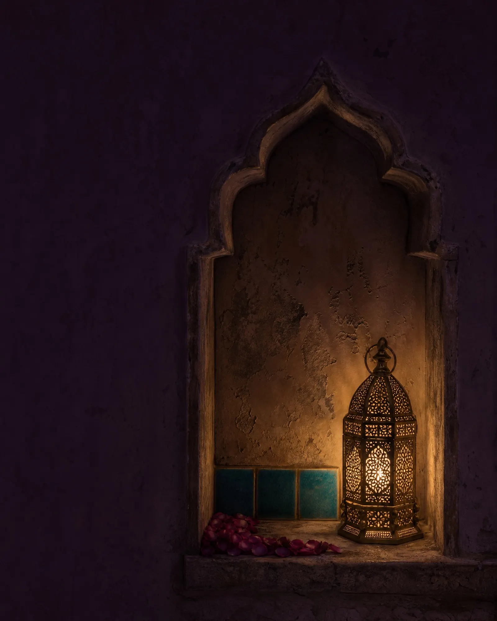 A single pierced lantern glows within a weathered plaster niche above turquoise tile.